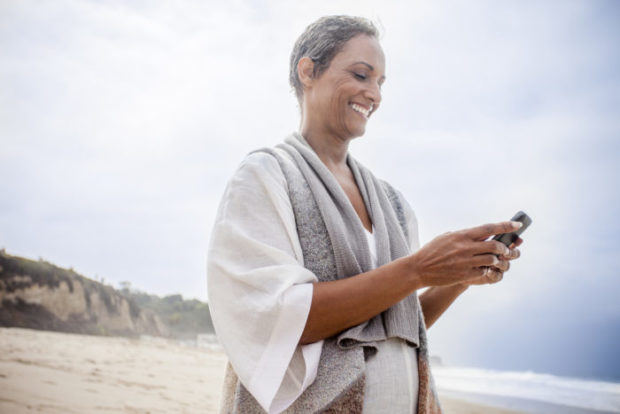 A senior African American woman checks her phone on the beach.